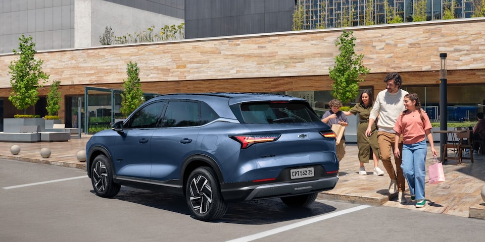 Chevrolet Captiva PHEV estacionada en la puerta de un local comercial mientras una familia se aproxima a ella para guardar bolsas de compras.