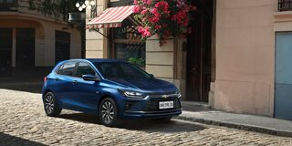 Chevrolet Onix Azul Boreal estacionado em rua de paralelepípedo, com fachada florida ao fundo.