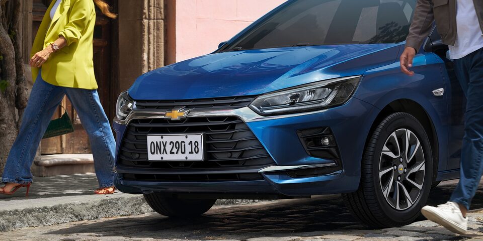 Vista frontal do Onix Azul Boreal com pessoas passando ao lado do veículo.