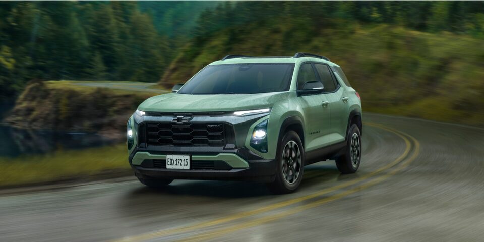 Chevrolet Equinox Activ Turbo visto de frente e lateral direita, em movimento em estrada sinuosa com vegetação ao fundo.