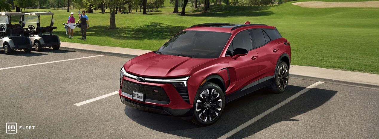 Chevrolet Blazer EV RS vermelho em um estacionamento ao ar livre, com área verde e árvores ao fundo