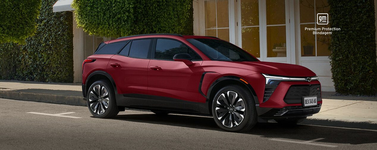 Blazer EV RS vermelha estacionada na rua. No canto superior direito, o selo GM – Premium Protection Blindagem.