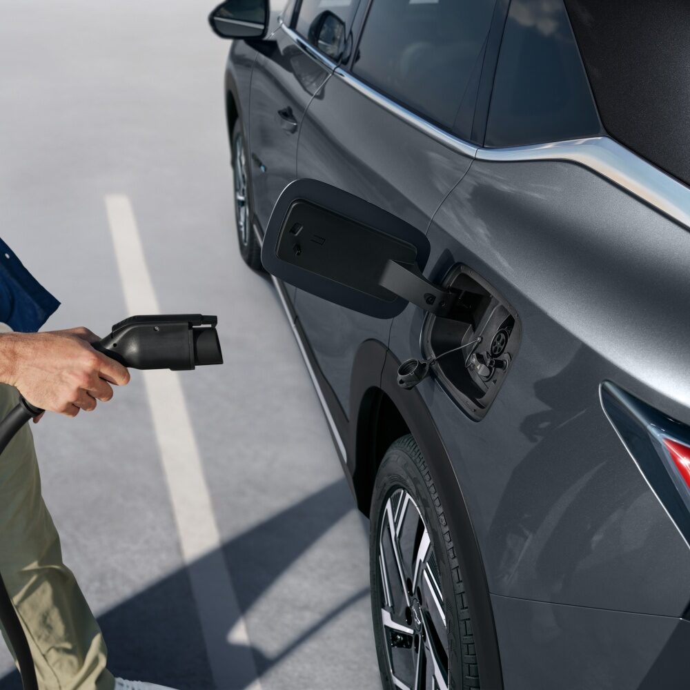 Pessoa conectando o cabo de carregamento em um SUV Chevrolet Captiva EV estacionado, mostrando o detalhe da porta de recarga elétrica.