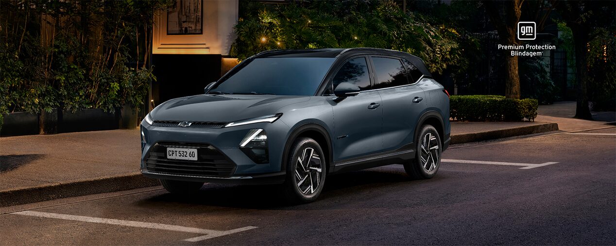 Chevrolet Captiva EV 2026 estacionado em uma rua urbana à noite, com vegetação e fachada iluminada ao fundo. O texto destaca Captiva EV 2026.