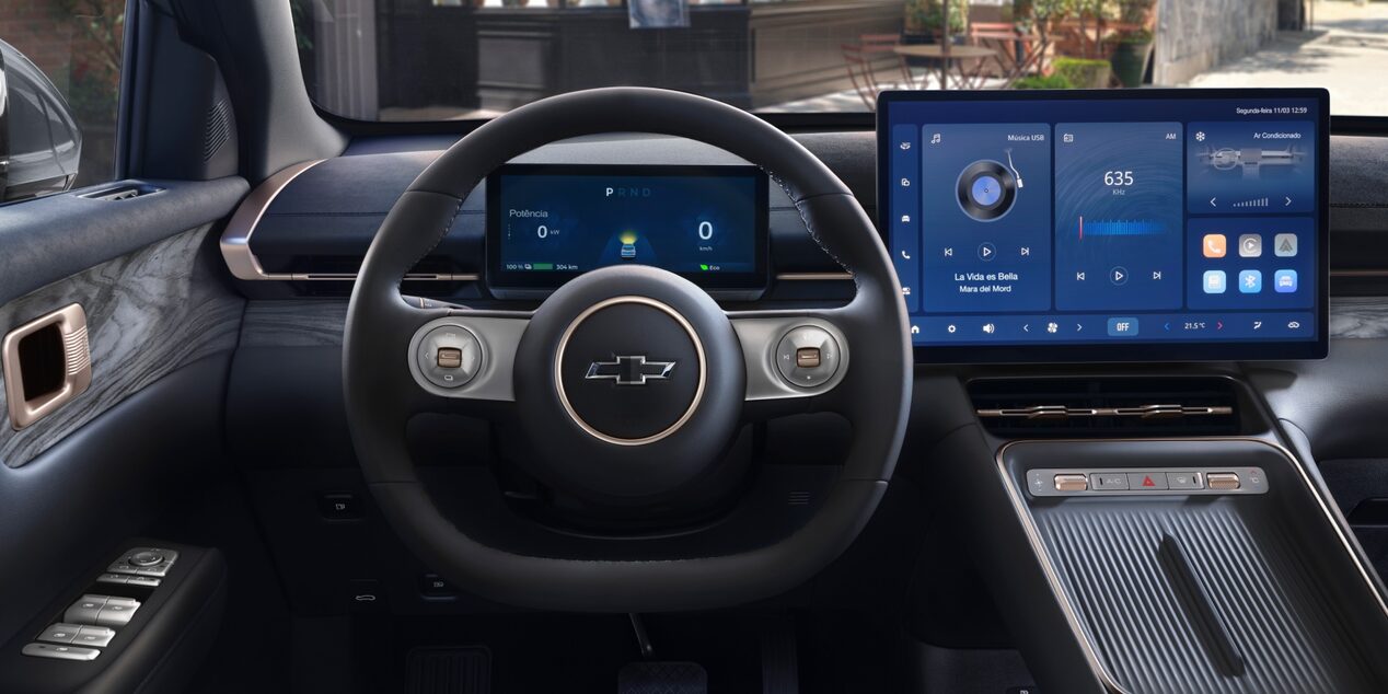 Interior do SUV Chevrolet Captiva EV, mostrando o volante com o logotipo da Chevrolet e o painel digital com duas telas grandes de comando e entretenimento.