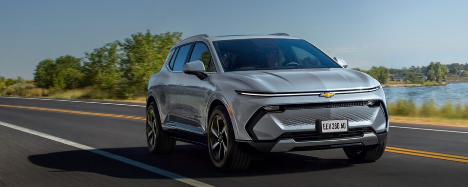 Chevrolet Equinox EV 2024 em movimento em uma estrada, com céu azul ao fundo e destaque para opção de assinatura mensal.