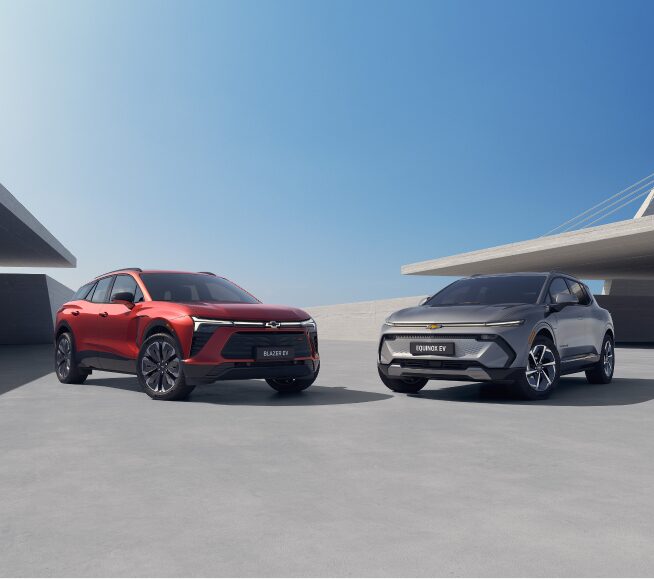 Banner predominantemente azul. À esquerda, um quadrante azul escuro com o logo GM Fleet no alto; abaixo, o texto: Assine seu Chevrolet - Dirigir um Chevrole 0 km com tudo incluso ficou mais simples. Com a assinatura GM Fleet, pessoas físicas e jurídicas contam com um pacote completo: seguro, IPVA, licenciamento e manutenção já estão resolvidos. E quando o contrato termina, é só trocar de carro e continuar rodando com praticidade, além do CTA (botão) de Sabia mais. À direita, um Blazer EV RS na cor vermelha e um Equinox EV na cor prata, em imagem ambientada.