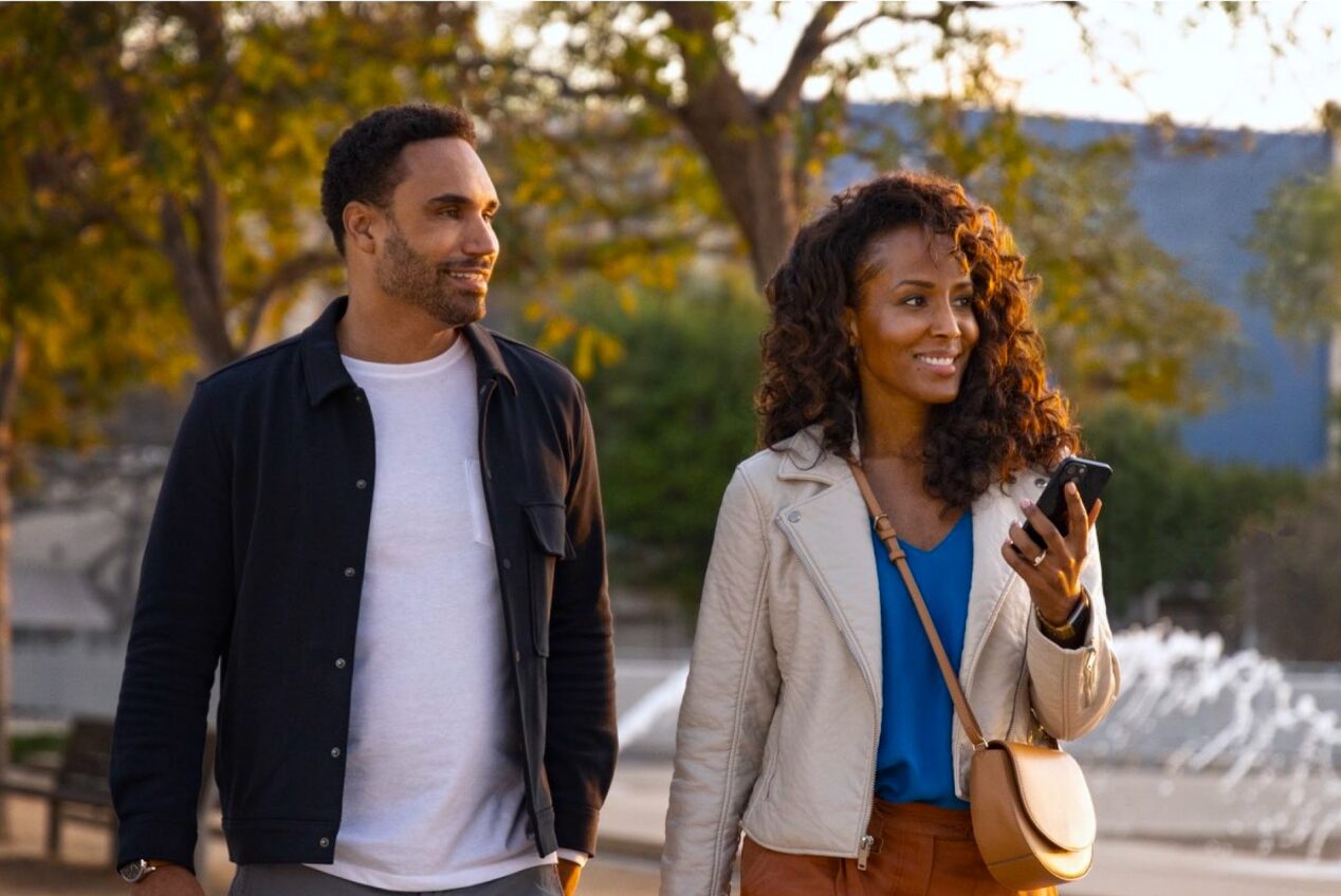 Dois jovens negros, um homem e uma mulher com um celular na mão