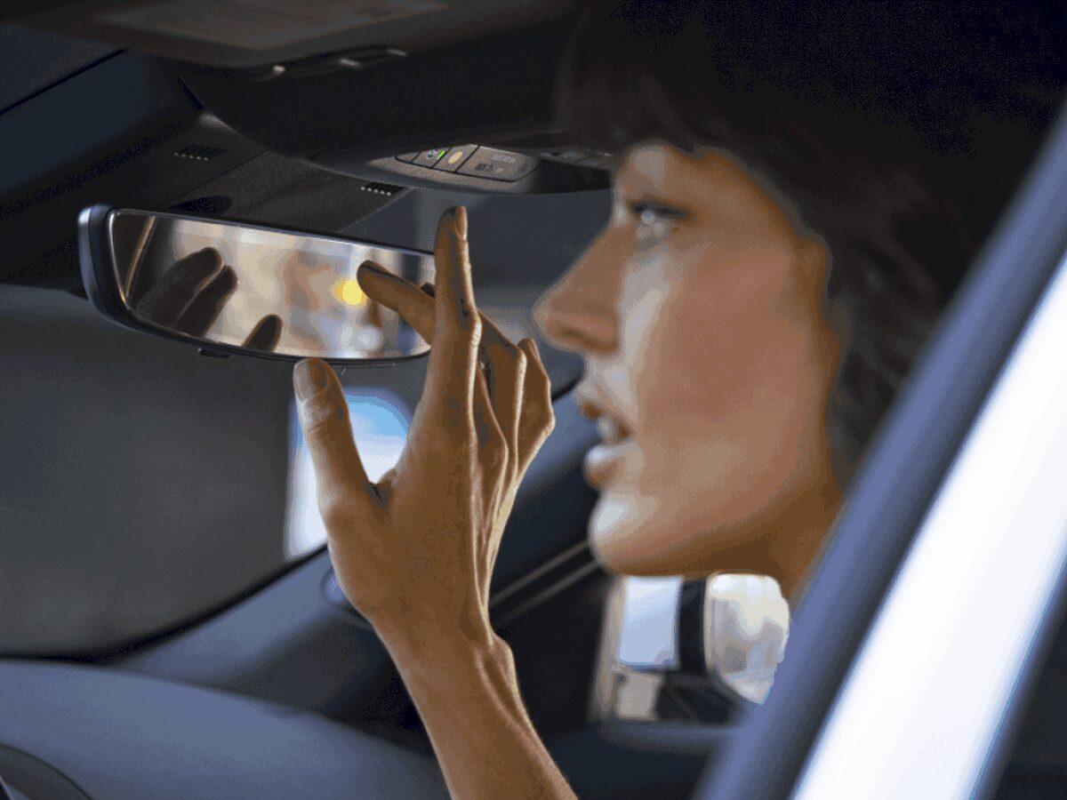 Mulher ajustando o retrovisor interno do carro enquanto está sentada no banco do motorista.