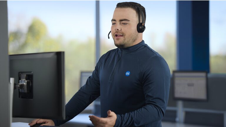Um atendente de suporte técnico com headset trabalha em frente ao computador em um ambiente de escritório moderno, pronto para auxiliar clientes.