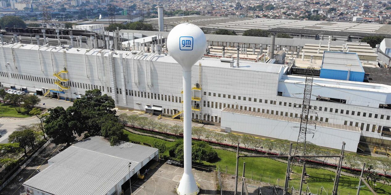 Vista aérea da fábrica da General Motors em São Caetano do Sul, com destaque para a caixa d’água branca com logotipo GM em primeiro plano e o complexo industrial ao fundo.