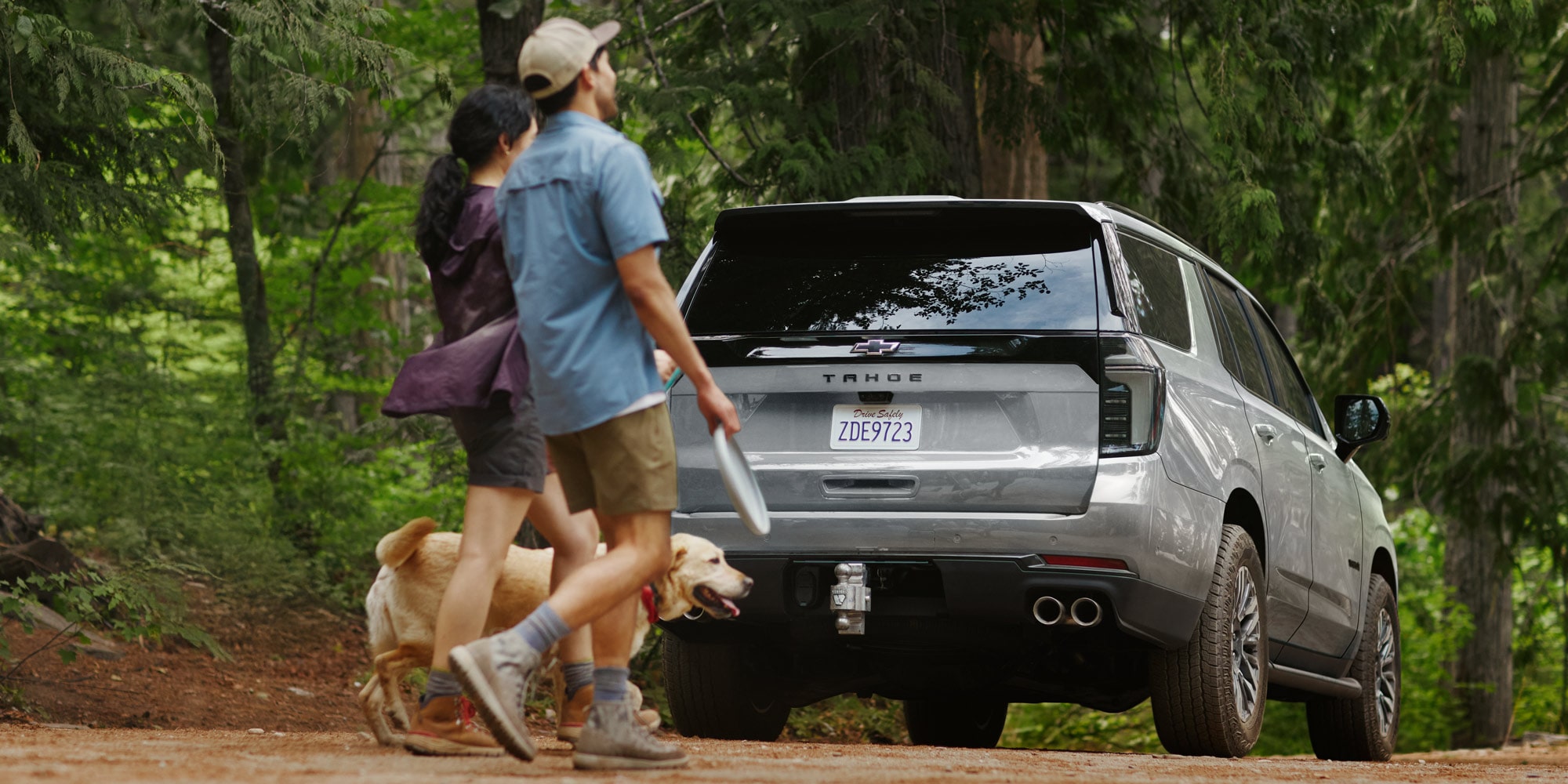 Chevrolet Tahoe estacionada en un camino de tierra con una pareja paseando un perro cerca.