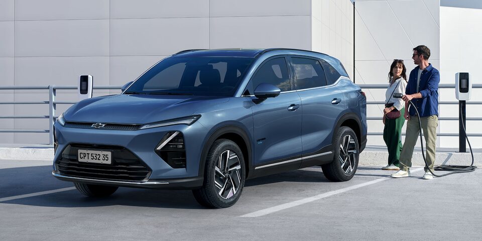 Imagen de un hombre y una mujer a punto de cargar una Chevrolet Captiva PHEV estacionada en una playa de estacionamiento con cargadores eléctricos.