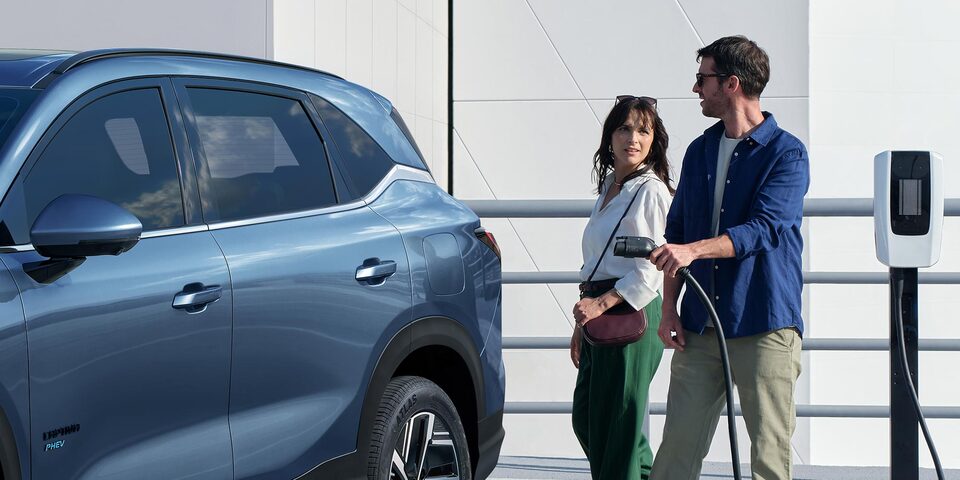 Imagen de un hombre y una mujer a punto de cargar una Chevrolet Captiva PHEV estacionada en una playa de estacionamiento con cargadores eléctricos.