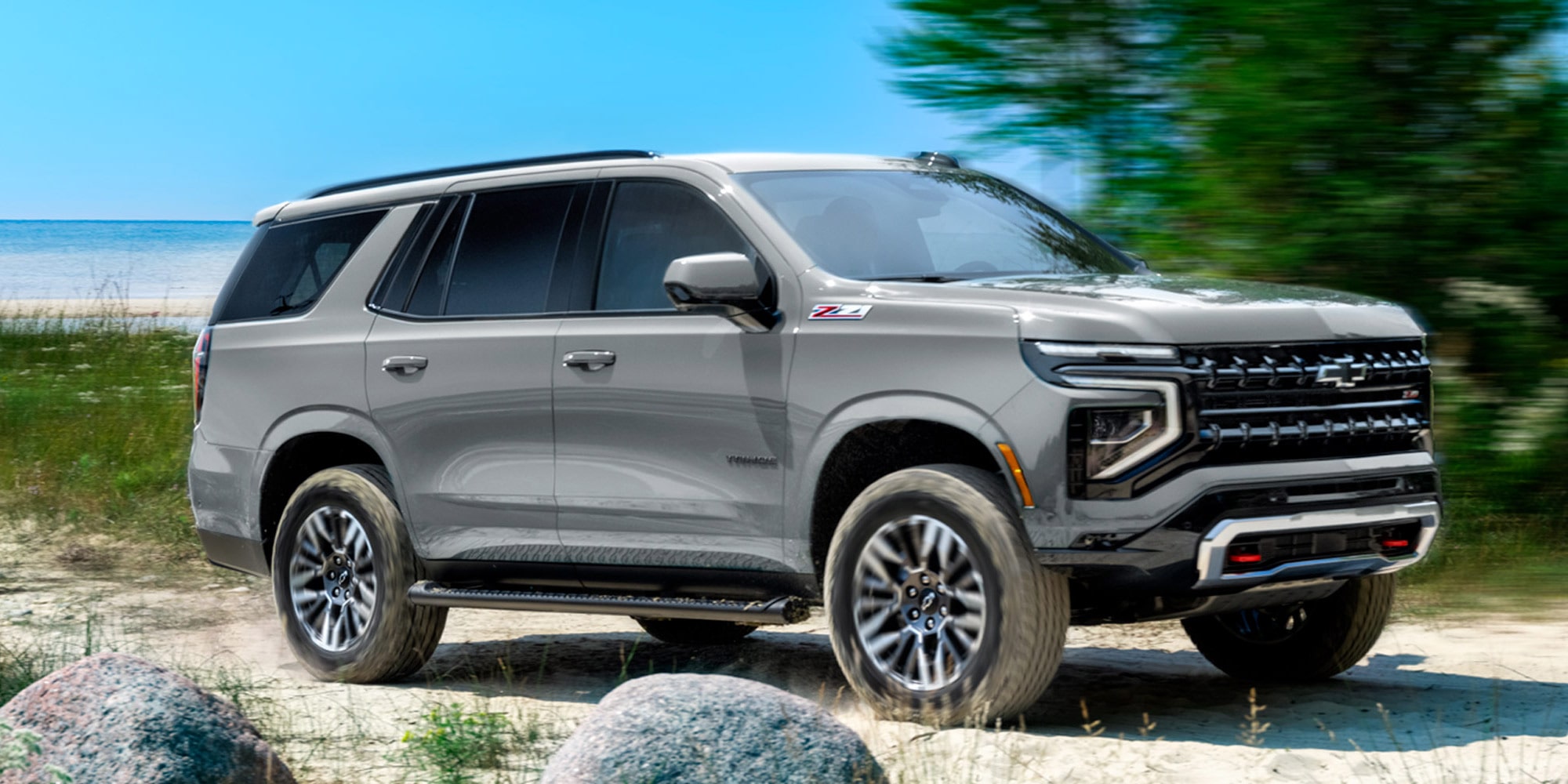 Chevrolet Tahoe andando sobre un camino de arena, con árboles y el mar de fondo.