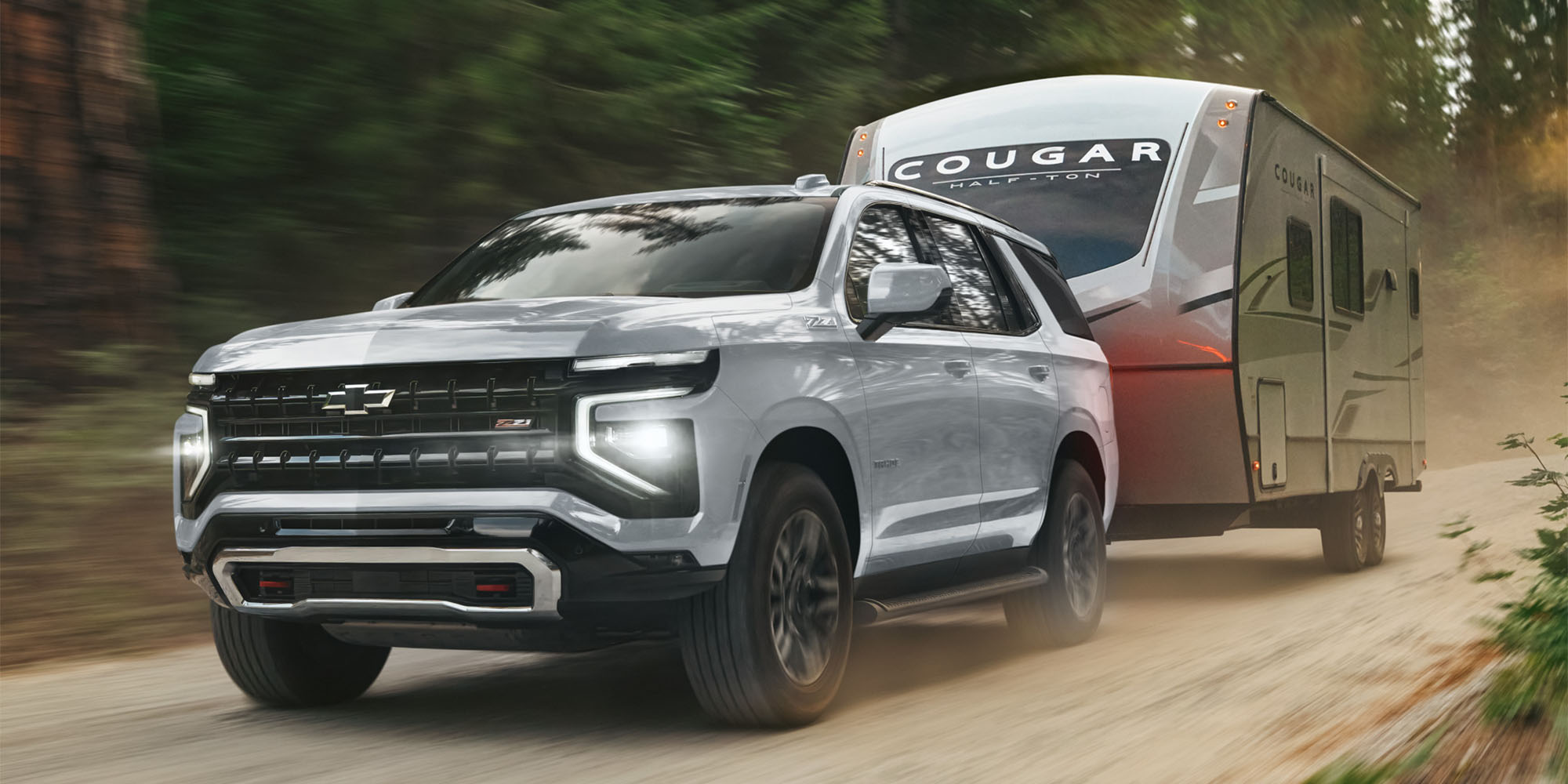 Chevrolet Tahoe remolcando un trailer por un camino de tierra en medio del bosque.