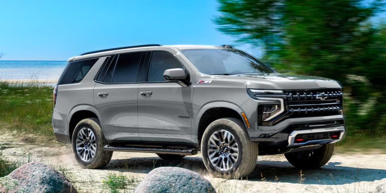 Chevrolet Tahoe andando sobre un camino de arena, con árboles y el mar de fondo.