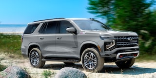 Chevrolet Tahoe andando sobre un camino de arena, con árboles y el mar de fondo.