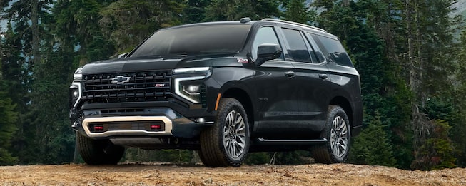 Chevrolet Tahoe SUV negra todo terreno estacionada en un entorno natural con árboles, destacando su robustez