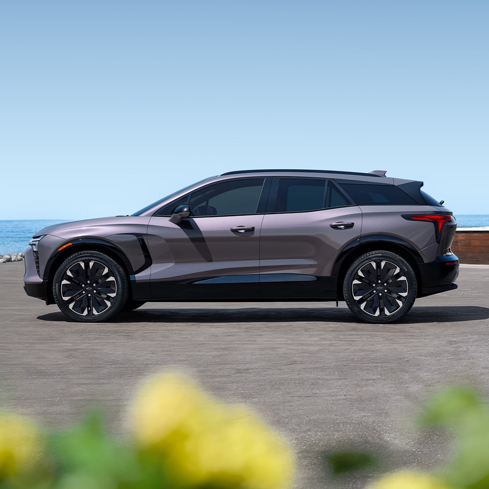 Una Chevrolet Blazer EV estacionada, mientras al fondo se ve el mar y unas flores desenfocadas en primer plano.